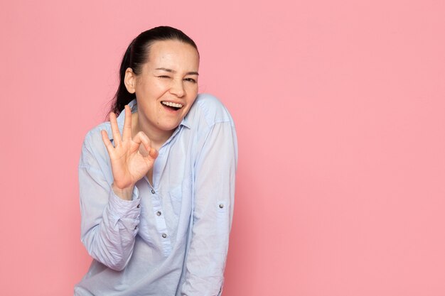giovane femmina in camicia blu in posa sul muro rosa