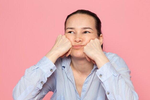 giovane femmina in camicia blu in posa sul muro rosa