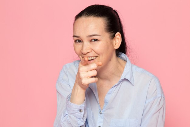 giovane femmina in camicia blu in posa sul muro rosa