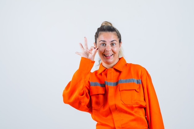 Giovane femmina in uniforme del lavoratore che mostra gesto giusto e che sembra felice, vista frontale.