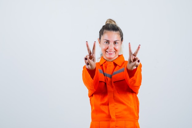 Giovane femmina in uniforme del lavoratore che mostra v-segno e che sembra felice, vista frontale.