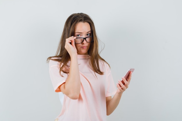 Giovane femmina utilizzando il telefono cellulare, togliendosi gli occhiali in maglietta rosa, vista frontale.