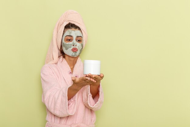 Giovane femmina vista frontale dopo la doccia in accappatoio rosa che tiene crema sulla superficie verde