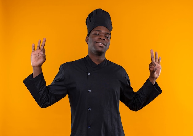 Giovane fiducioso afro-americano cuoco in chef uniforme gesti okmhand segno con entrambe le mani isolato su sfondo arancione con copia spazio