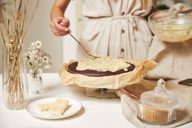 Giovane fornaio femminile che prepara una deliziosa torta al cioccolato con crema su un tavolo bianco