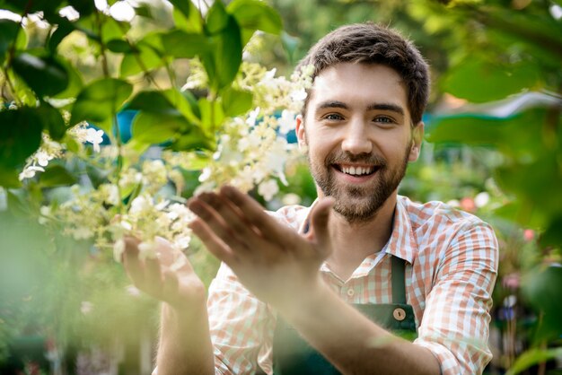 Giovane giardiniere allegro bello che sorride, prendendosi cura dei fiori