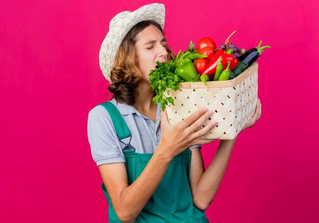 Giovane giardiniere uomo che indossa tuta e cappello tenendo la cassa piena di verdure fresche