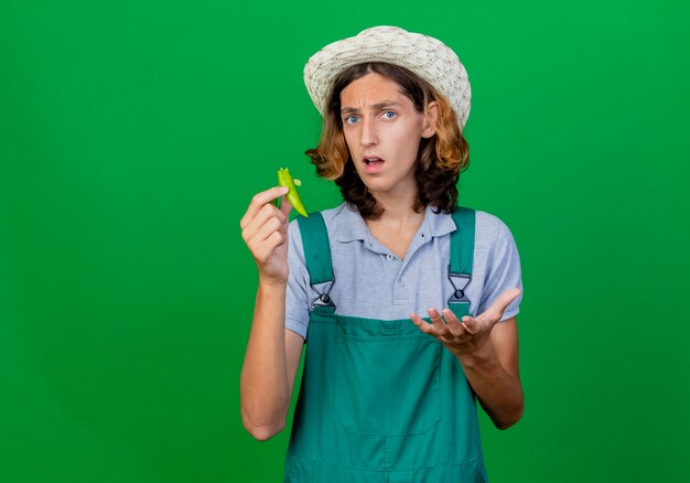 Giovane giardiniere uomo che indossa tuta e cappello tenendo le metà del peperoncino verde