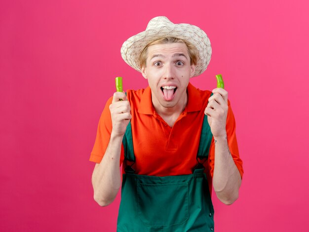 Giovane giardiniere uomo che indossa tuta e cappello tenendo le metà del peperoncino verde