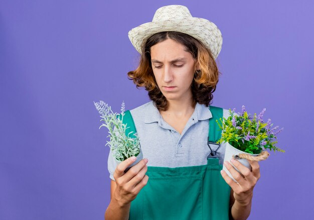 Giovane giardiniere uomo che indossa tuta e cappello tenendo le piante in vaso