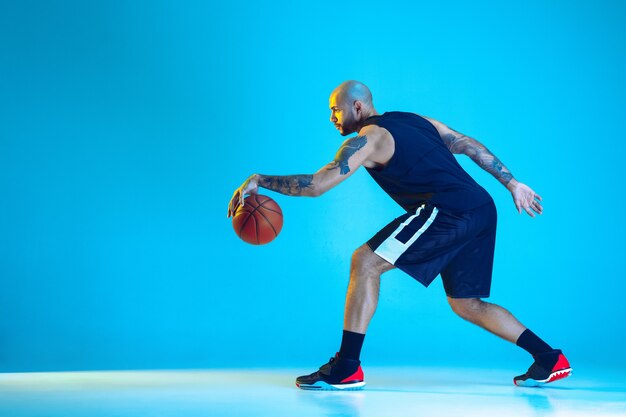 Giovane giocatore di basket della squadra che indossa l'allenamento sportivo, praticando in azione, isolato sulla parete blu in luce al neon