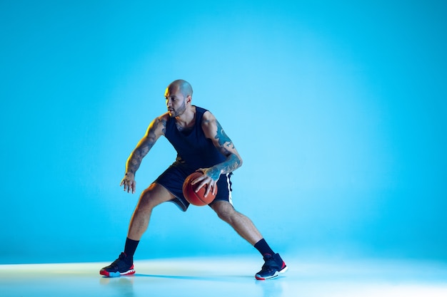 Giovane giocatore di basket della squadra che indossa l'allenamento sportivo, praticando in azione, isolato sulla parete blu in luce al neon