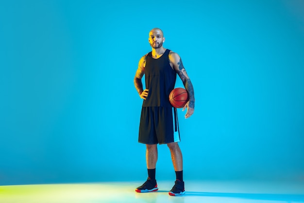 Giovane giocatore di basket della squadra che indossa la formazione di abbigliamento sportivo, pratica in azione, movimento sulla parete blu in luce al neon
