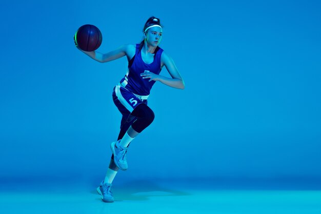 Giovane giocatore di basket femminile caucasico isolato su studio blu in luce al neon