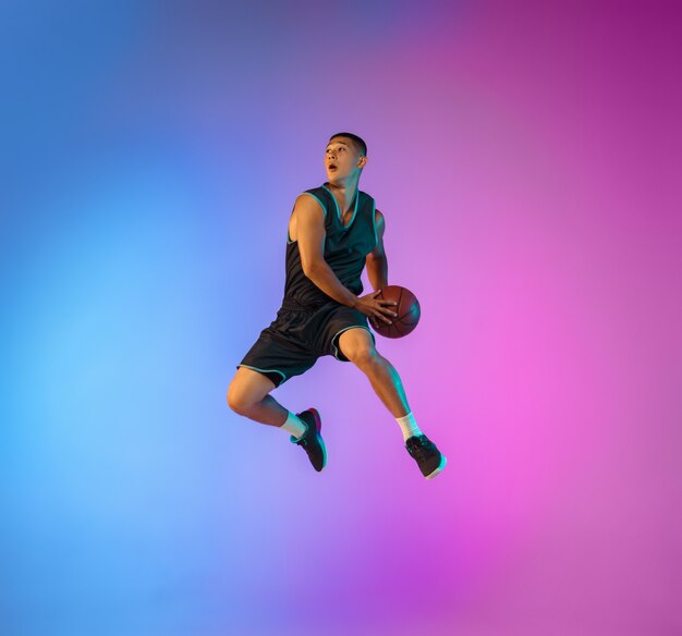 Giovane giocatore di basket in movimento sul gradiente di sfondo per studio in luce al neon
