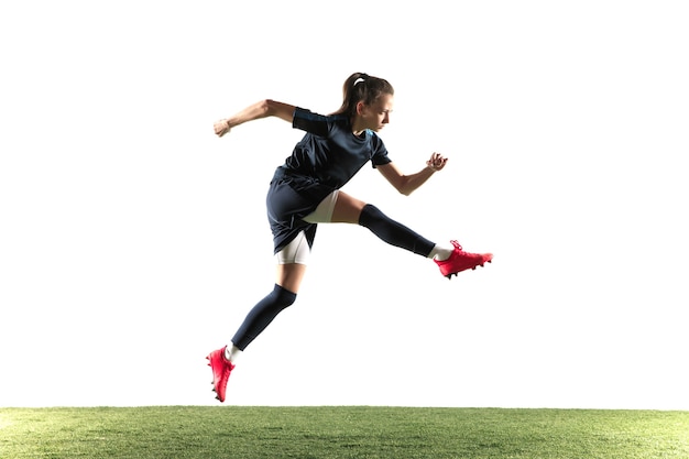 Giovane giocatore di calcio o di calcio femminile con i capelli lunghi in abbigliamento sportivo e stivali calciare la palla per l'obiettivo nel salto isolato su priorità bassa bianca. Concetto di stile di vita sano, sport professionistico, hobby.