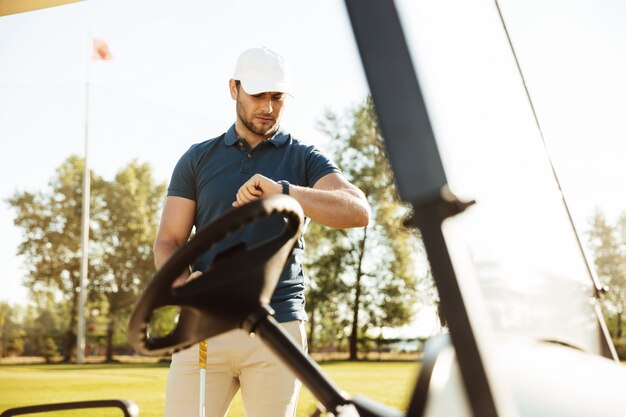 Giovane giocatore di golf maschio che esamina un orologio