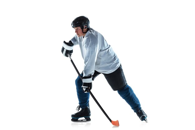 Giovane giocatore di hockey maschio con il bastone sul campo da ghiaccio e muro bianco