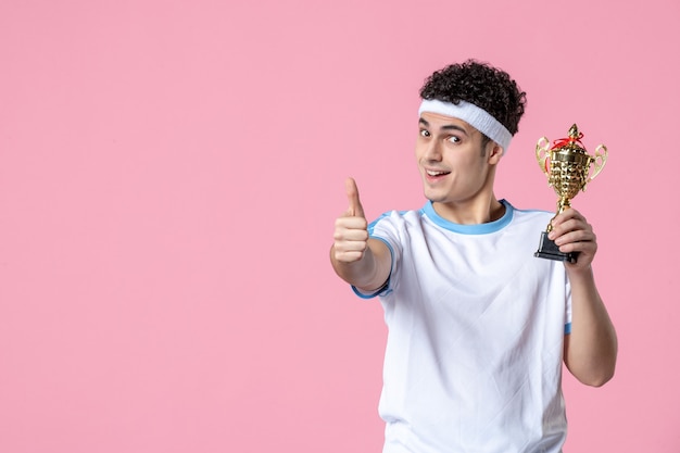 Giovane giocatore di vista frontale in vestiti di sport con la tazza dorata sulla parete rosa