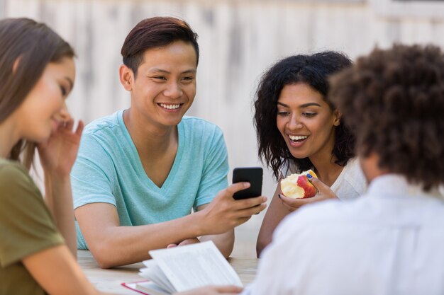 Giovane gruppo multietnico allegro di studenti degli amici che parlano facendo uso del telefono