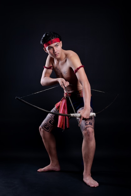 giovane guerriero maschio della TAILANDIA che posa in una posizione di combattimento con un arco sul nero