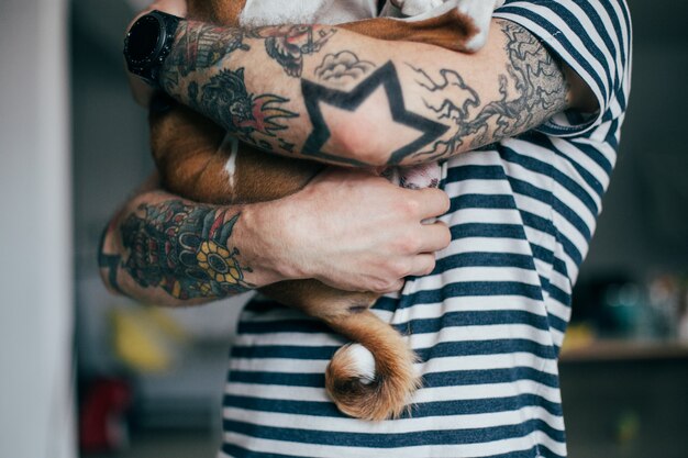 Giovane hipster alla moda con tatuaggi capelli ricci pazzi coccola il suo piccolo migliore amico