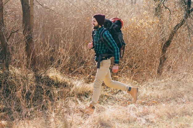 Giovane hipster che viaggia con lo zaino nella foresta autunnale indossando camicia e cappello a scacchi