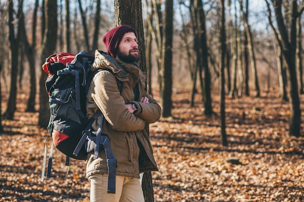 Giovane hipster che viaggia con lo zaino nella foresta autunnale indossando giacca e cappello caldi