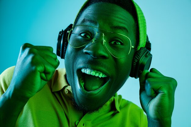 giovane hipster uomo che ascolta musica con le cuffie in studio blu con luci al neon. Espressione emotiva