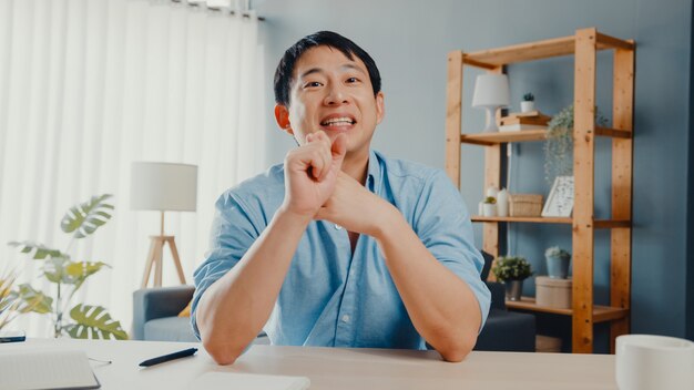 Giovane imprenditore asiatico utilizzando il computer portatile parlare con i colleghi del piano in videochiamata riunione mentre si lavora da casa