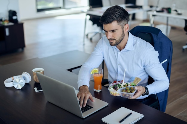 Giovane imprenditore che lavora al computer portatile mentre fa la pausa pranzo in ufficio