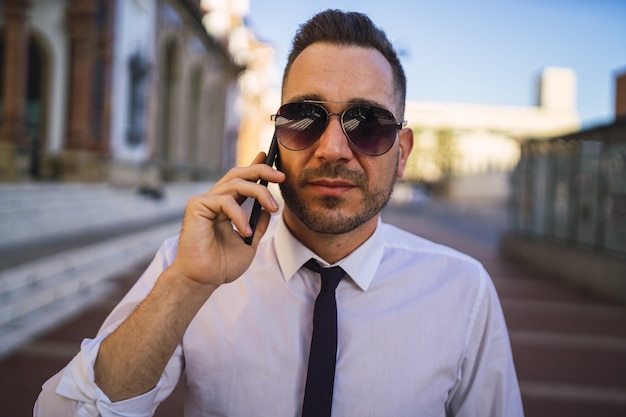 Giovane imprenditore di successo in un abito formale con occhiali da sole, parlando al telefono