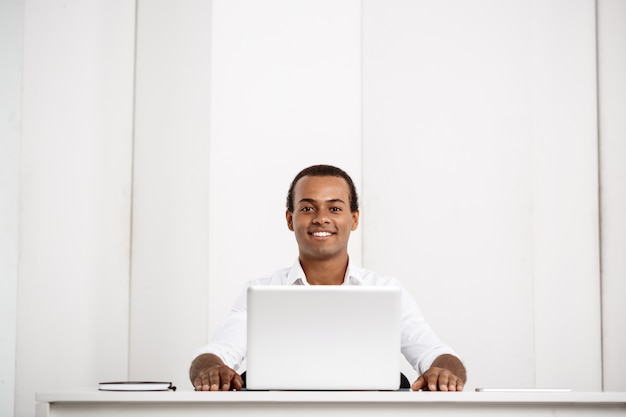 Giovane imprenditore di successo sorridente, seduto sul posto di lavoro con il portatile