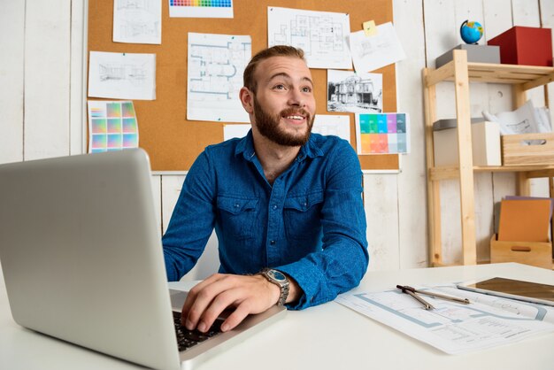 Giovane imprenditore di successo sorridente, seduto sul posto di lavoro con il portatile