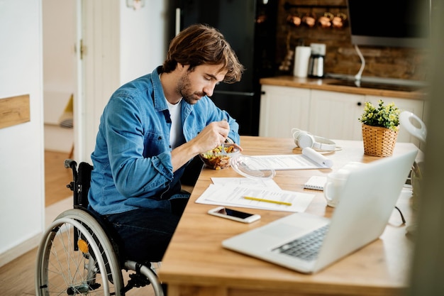 Giovane imprenditore in sedia a rotelle che fa pausa pranzo mentre lavora a casa