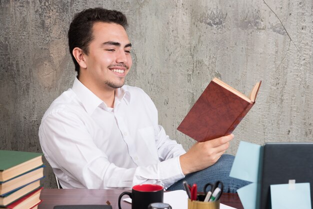 Giovane imprenditore leggendo un libro con felice espressione.