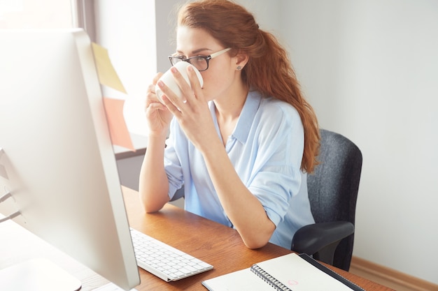 Giovane imprenditrice leggendo qualcosa sul computer mentre si gusta il caffè