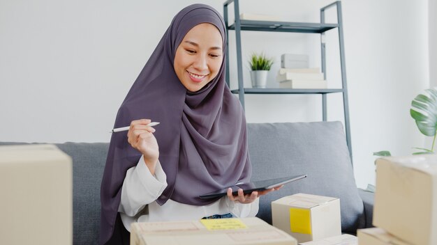 Giovane imprenditrice musulmana controlla l'ordine di acquisto del prodotto in magazzino e salva sul lavoro del computer tablet a casa.