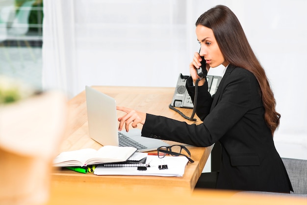 Giovane imprenditrice parlando sul telefono guardando portatile in ufficio