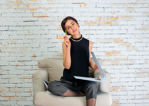 Giovane imprenditrice seduta sulla poltrona e tenendo penna e taccuino Foto di alta qualità
