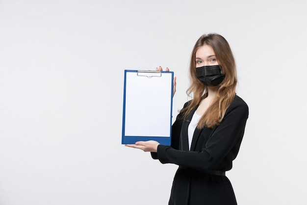 Giovane imprenditrice sicura di sé in tuta che indossa la sua maschera medica e mostra documenti sul muro bianco