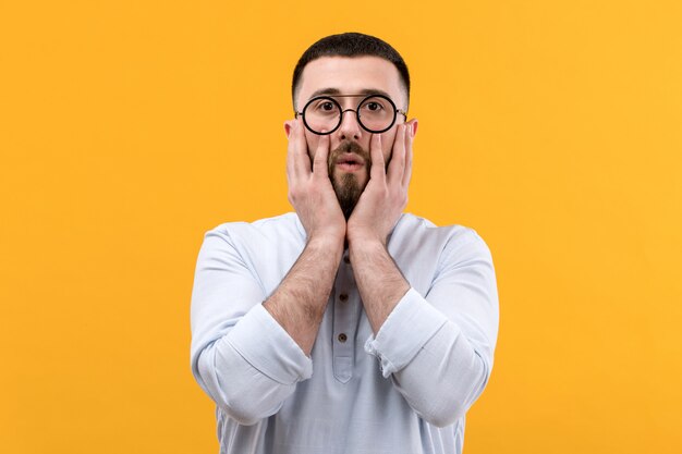 Giovane in camicia bianca con barba e occhiali con espressione sorpresa