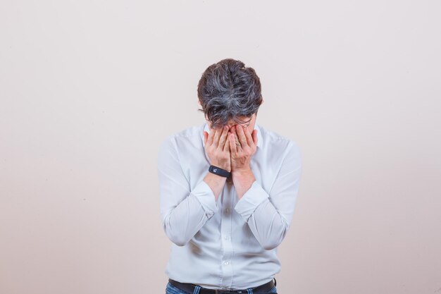 Giovane in camicia bianca, jeans che copre il viso con le mani e sembra sconvolto