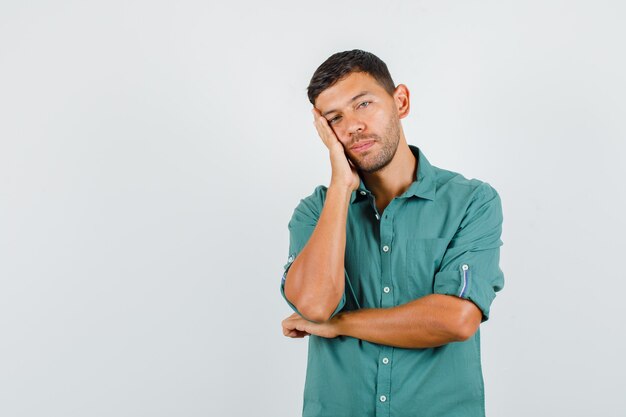 Giovane in camicia che si appoggia sulla guancia sul palmo sollevato e sembra stanco