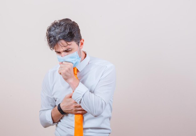 Giovane in camicia, cravatta, maschera che soffre di tosse e sembra malato un