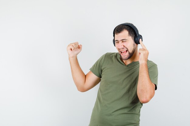 Giovane in maglietta verde che gode della musica con il gesto del vincitore e che sembra allegro