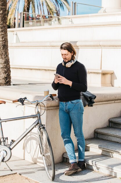 Giovane in piedi vicino alla sua bicicletta tramite smartphone