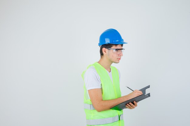 Giovane in uniforme da costruzione che scrive note nella cartella dei file e sembra concentrato