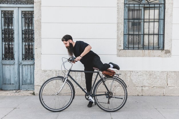 Giovane in vestiti neri che si siede sulla bicicletta per la strada