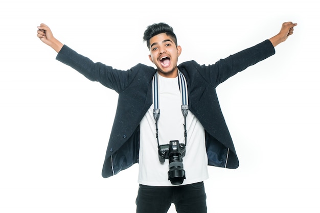 Giovane indiano bello con una macchina fotografica con le mani sollevate su fondo bianco